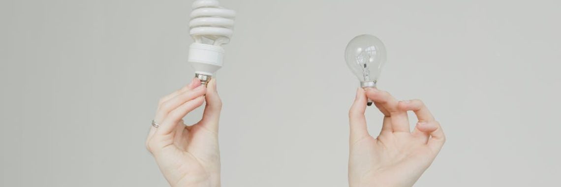 Hands hold incandescent and spiral light bulbs, symbolizing energy efficiency.