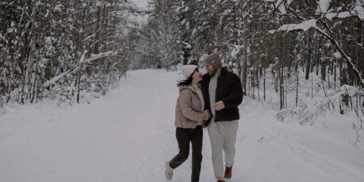 A joyful couple strolls through a snowy forest, embracing winter's beauty and tranquility.