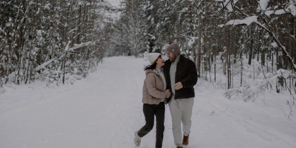 A joyful couple strolls through a snowy forest, embracing winter's beauty and tranquility.
