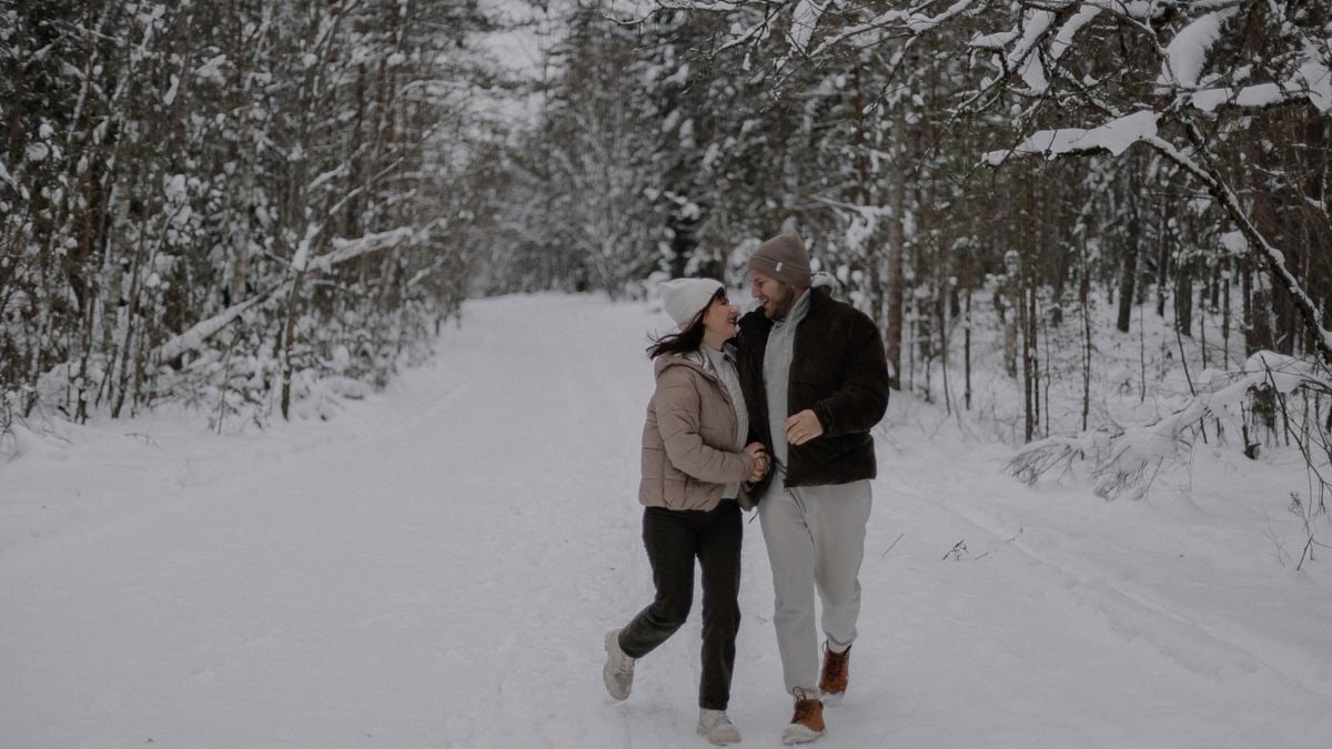 A joyful couple strolls through a snowy forest, embracing winter's beauty and tranquility.