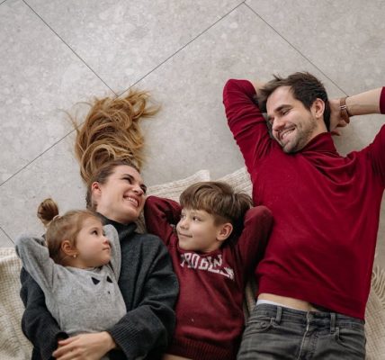 Smiling family of four lying on a blanket, sharing happiness and love indoors.