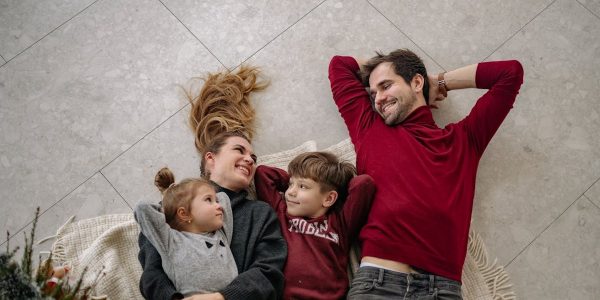 Smiling family of four lying on a blanket, sharing happiness and love indoors.