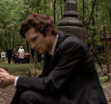 A man in mourning at a funeral surrounded by gravestones in a serene forest cemetery.