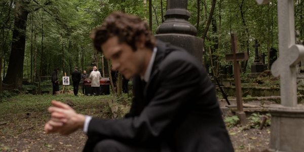 A man in mourning at a funeral surrounded by gravestones in a serene forest cemetery.
